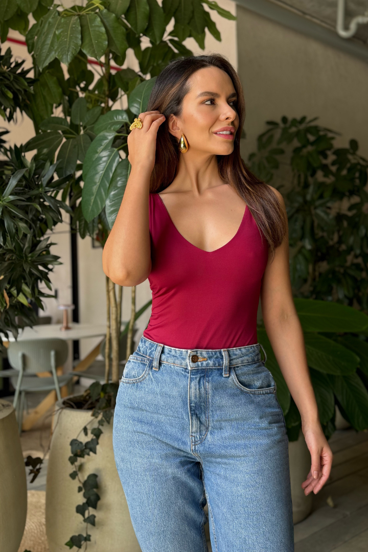 Modelo colombiana con body Ryna vino de escote en V y jeans, luciendo aretes dorados, cómoda y empoderada.