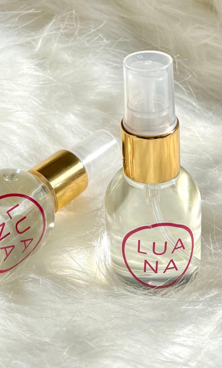 Primer plano de dos botellas de fragancia Folgora de 49 ml con pulverizador dorado, etiqueta Luana, sobre fondo blanco peludo.