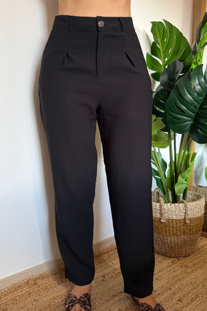 Pantalón Vera negro de pierna ancha con pliegues frontales, de cintura alta, sobre modelo con sandalias. Ideal para outfit casual o formal.