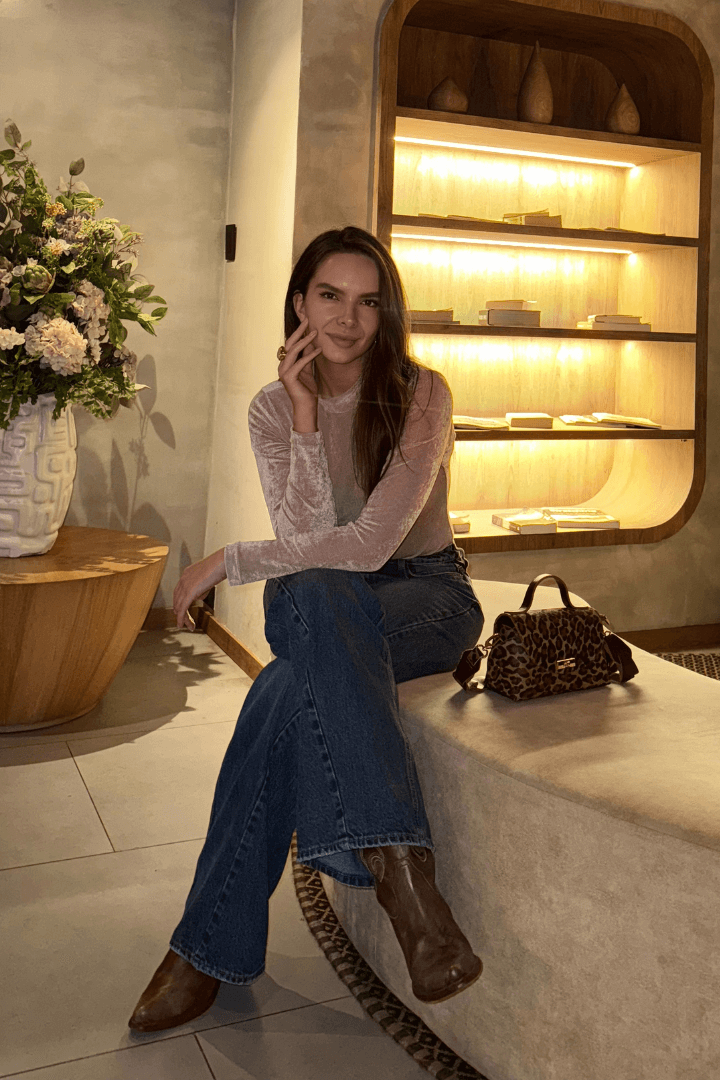 Modelo en Body Brisa palo de rosa mallatex, manga larga y cuello alto, con jeans y botas, sentada