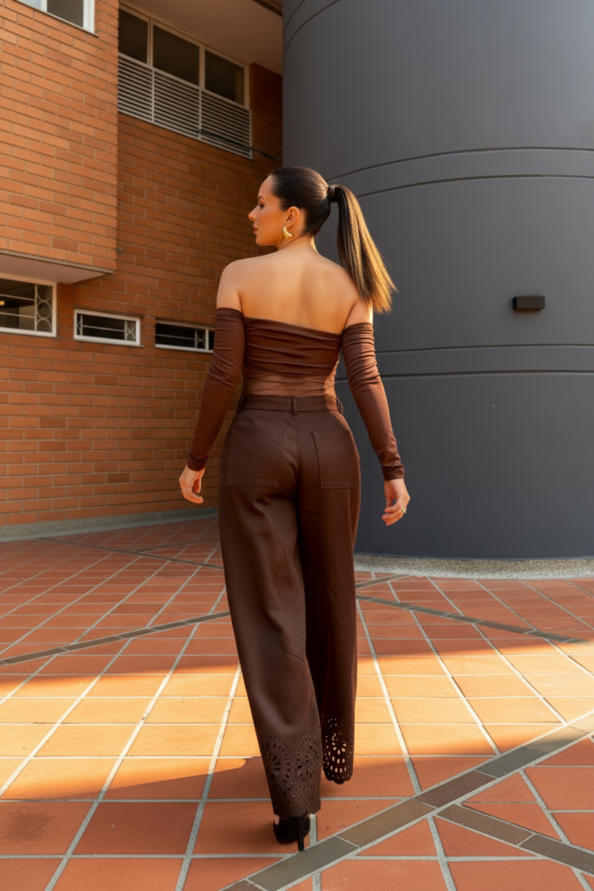 Body Aria Marrón: mujer con top marrón asimétrico y manga larga ruched, pantalón ancho, caminando en una plaza urbana.