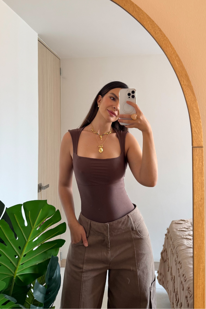 Mujer usando body Elsa Mocca control abdomen color café, reflejada en un espejo con planta verde al lado