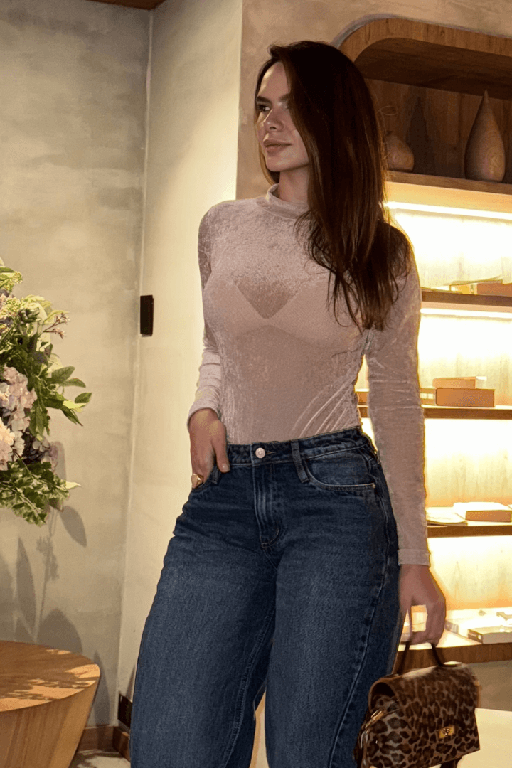 Modelo en body Brisa palo de rosa manga larga cuello alto de mallatex, con jeans oscuros y bolso estampado de leopardo.